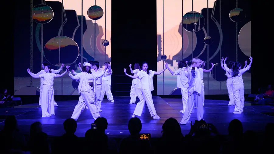 Dancers dressed in white hold their arms outstretched to the side, turning to face the audience