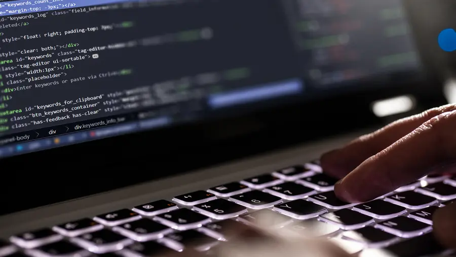 A close up of hands typing computer code on a keyboard.