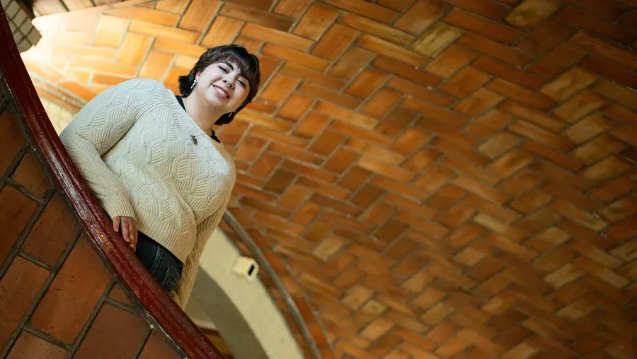 A smiling woman peers down from the stairwell in Baker Hall
